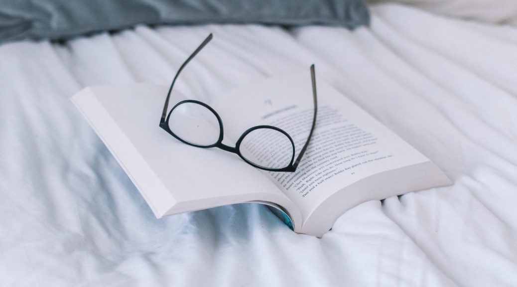 Book on bed with black glasses